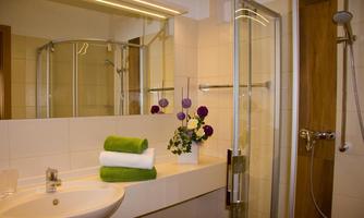 A modern bathroom with a shower cabin and bright tiles. Fresh towels and a flower arrangement create an inviting atmosphere.