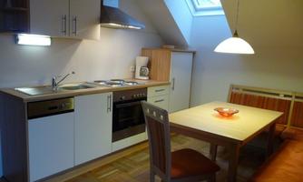 A modern kitchen with bright furniture and appliances. A dining table with chairs and a cozy seating area is also present.