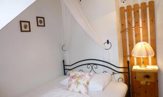 A cozy bedroom with an iron bed and a bedside table. The walls are light, and there are some decorations that create an inviting atmosphere.