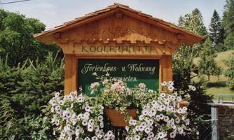 A beautiful wooden sign with the inscription "Koglerhütte". Surrounded by colorful flowers and green trees.