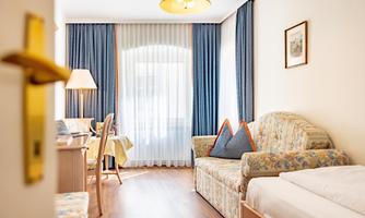 A bright room with a cozy sofa and a work desk. The windows are framed by curtains that let in plenty of daylight.