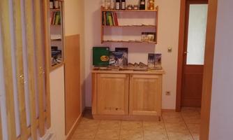 A cozy hallway with a wooden ceiling and tiled floor. Shelves with drinks and brochures are standing against the walls.