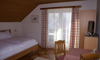 A cozy room with a double bed and a table. Large windows let in plenty of light and offer a view of the outside.