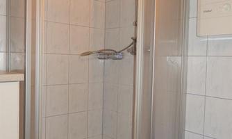 A shower cubicle with transparent doors stands in a bathroom. Next to the shower is a blue laundry basket.