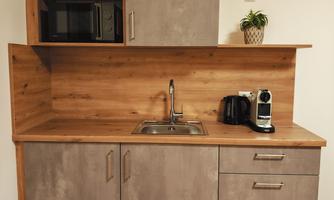 A modern kitchenette with a combination of gray tones and wood. It includes a microwave, a coffee machine, and a sink.