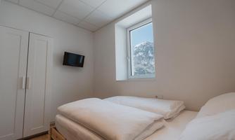 A simple and bright room with two single beds. A mountain landscape can be seen through the window.