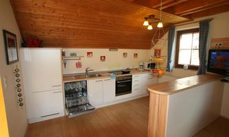 A modern kitchen with a wooden ceiling and bright furnishings. It is well equipped with a dishwasher, stove, and microwave.