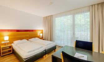 A modern hotel room with two beds and a desk. Large windows let in plenty of light and offer a view of the surroundings.