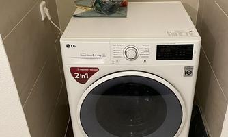 A washing machine in a small laundry room with a tiled floor. On the machine, there is a bottle and some accessories.
