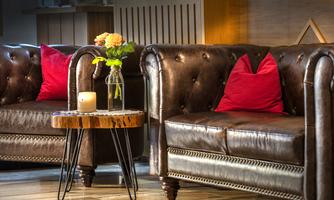 Two elegant leather sofas with red cushions are situated in a stylish room. A small table with a flower vase and a candle stands between the sofas.