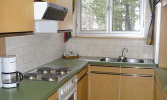 A modern kitchen with wooden cabinets and a green workspace. A large window provides plenty of daylight.