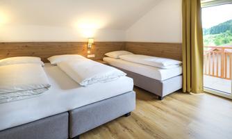 A cozy bedroom with two beds and wooden panels. Large windows provide a view of the green landscape.