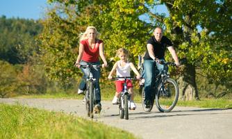 A family is riding bicycles on a picturesque path. The parents and the child are enjoying nature and the sunny weather.