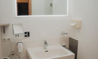 A modern bathroom with a sink and a lit mirror. The walls are bright and the decor is simple and functional.