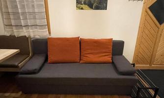 A cozy gray sofa with orange cushions in a rustic room. In the background, there is a picture of mountains.