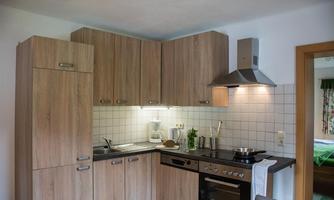A cozy kitchen with wooden cabinets and modern appliances. There is a sink, a stove, and windows that let in natural light.