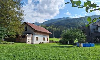 A typical country house surrounded by green meadows and trees. In the background, gentle hills and a blue sky with clouds can be seen.
