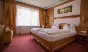 A cozy room with a double bed and light wooden furniture. Large windows let in plenty of daylight.