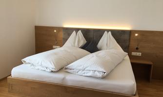 A modern bedroom with a double bed and two large pillows. The walls are in neutral colors, and the wood design conveys a warm atmosphere.