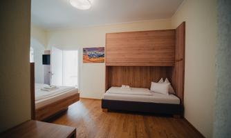 A modern room with two beds and hardwood floor. A picture hangs on the wall, and there is plenty of natural light.