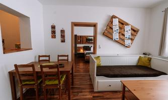 A cozy apartment with a dining table and chairs. The decor is modern and bright, featuring a narrow sofa and decorative elements on the wall.