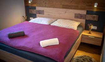 A cozy bedroom with a double bed and wooden paneling. The bedding is colorful, and there are two towels on the bed.
