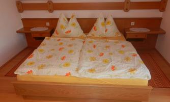 A cozy bedroom with a double bed and two pillows. The duvet has a floral pattern and there are two nightstands against the wall.
