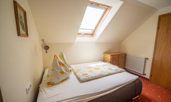 A cozy bedroom with a slanted skylight. The bed is simple and equipped with a colorful bedspread.