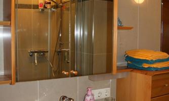A modern bathroom with a marble sink and a large mirror. In the background, a shower is visible and some grooming products are placed on the table.