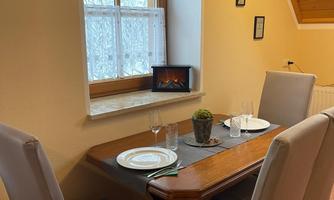 A cozy dining area with a table and two chairs. Natural light is shining through the window, and in the background, there is a small decoration.