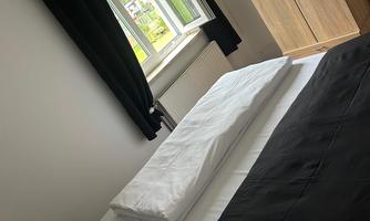 A bedroom with a large window and a wardrobe. On the bed are black and white bedspreads.