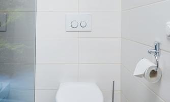 A modern bathroom with a white toilet and clean lines. The walls are tiled in neutral tones, and there is a towel rack.