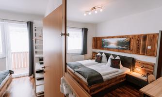A cozy bedroom with wooden details and modern furniture. The room features a large window and offers a warm, inviting atmosphere.