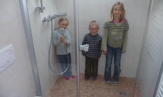 Three children are standing in a shower. The room is brightly lit and modernly designed.