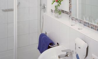 A modern bathroom with a shower and sink. The space is brightly tiled and decorated with a flower.