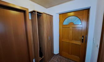A small hallway with a wooden door and a coat cupboard. The floor is tiled and the walls are painted light.