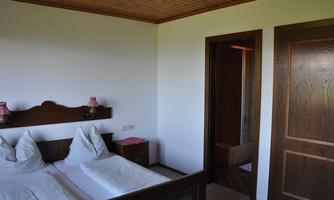 A simple bedroom with two beds and wooden decor. In the background, a door to a bathroom is visible.