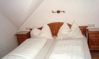 A cozy bedroom with a double bed and wooden dressers. The bedding is neat and the walls are painted white.