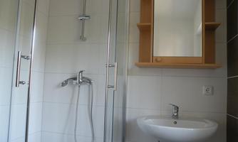 A modern bathroom with a shower and a sink. There is a mirror on the wall and there are bright, simple tiles.