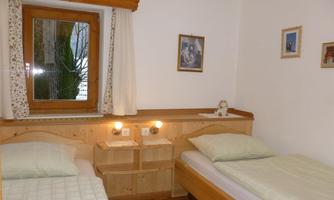 A cozy bedroom with two single beds and wooden-panelled walls. By a window, there are curtains and small picture frames visible.