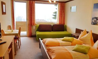 A cozy room with two beds and a green sofa.  
Large windows provide plenty of light and offer a view outside.