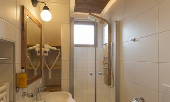 A modern bathroom with a shower, a sink, and a wall mirror. The walls are brightly tiled, and the ceiling has wood paneling.