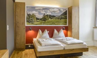 A cozy bedroom with a double bed and natural wooden paneling. A large picture of a picturesque landscape hangs on the wall.