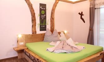 A cozy bedroom with a large bed and green bedding. The walls are adorned with wood details and decorative wall design.