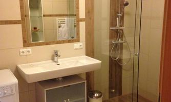 A modern bathroom with a glass shower enclosure and a sink. The walls are tiled in light colors and the floor is made of wood.