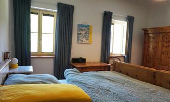 A cozy bedroom with a double bed and a wooden table.  
Large windows let in lots of daylight, and the curtains are in a deep blue color.