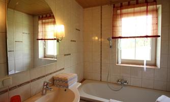 A modern bathroom with a bathtub and a sink. The window lets in natural light and there are towels on the shelf.