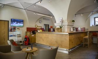 A modern reception hall with a wooden counter and comfortable seating. The walls are painted light, and there is a large television screen.
