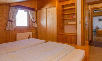 A cozy bedroom with wood paneling and two beds. The windows are decorated with curtains and a shelf is mounted on the wall.