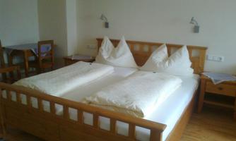 A cozy bedroom with a wooden bed and two single mattresses. Next to the bed are nightstands, and there is a small dining area with a table and chairs.